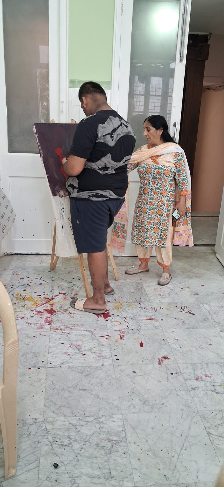Alma Studio artist painting at an easel while a mentor observes